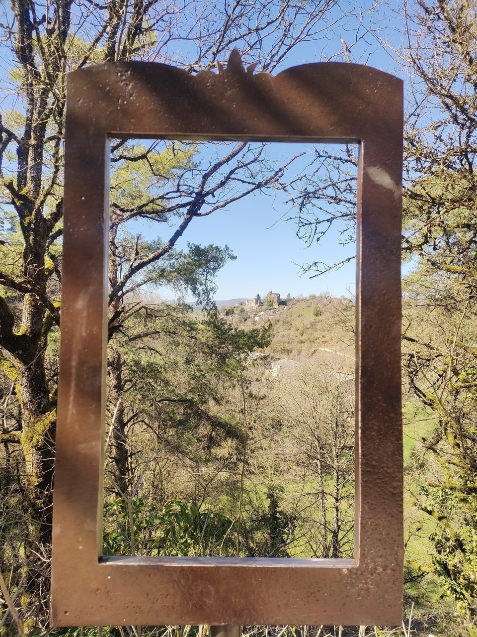 La Roque Valzergues au loin, vue à travers une création artisanale des locaux
